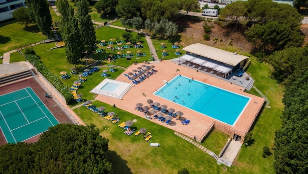 Luchtbeeld van een resort met een zwembad, ligbedden en een tennisbaan.