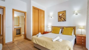 Een hotelkamer met een bed, nachtlampen, een schilderij en een zichtbare badkamer door een open deur.