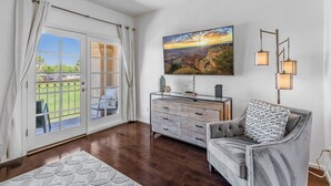 Ein geräumiges Wohnzimmer mit großem Fenster, einer bequemen Couch, einem Holzkasten und einem an der Wand hängenden Gemälde.