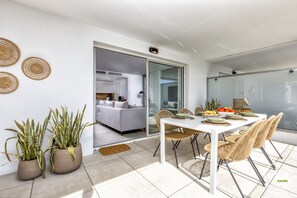 Uma sala de jantar moderna com mesa branca, cadeiras de vime e plantas em vasos.