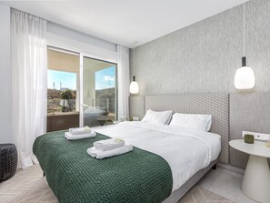 A modern hotel room with a large bed, a round side table, and a view of the outdoors.