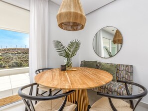 A modern dining area with a round wooden table, black chairs, a woven pendant light, a round mirror, and a potted plant.