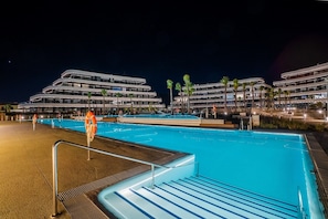 A swimming pool area with steps leading into the pool, surrounded by modern buildings with multiple floors and balconies.
