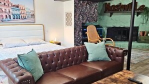Une chambre à coucher moderne avec un canapé en cuir marron, une table basse en bois, un ventilateur de plafond et un tableau représentant un paysage urbain.
