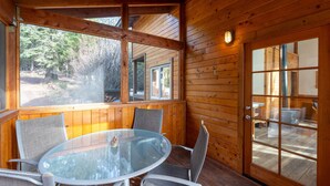 Een houten chalet met een glazen tafel en stoelen, grote ramen en een deur die leidt naar een buitenruimte.