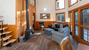 Een gezellig chaletinterieur met een open haard, houten wanden, een bank en grote ramen.