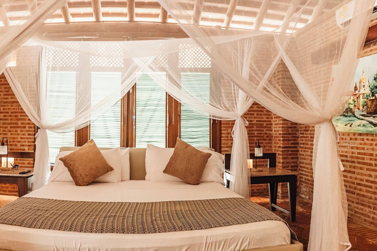 A bed with a canopy, a brick wall, and a painting on the wall.