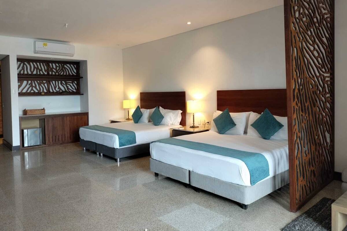 A hotel room with two beds, a minibar, a wooden decorative panel, and a ceiling-mounted air conditioner.
