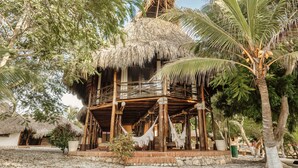 A wooden structure with a thatched roof, surrounded by palm trees and potted plants. - Castillete Hotel & Beach Club (Cartagena)