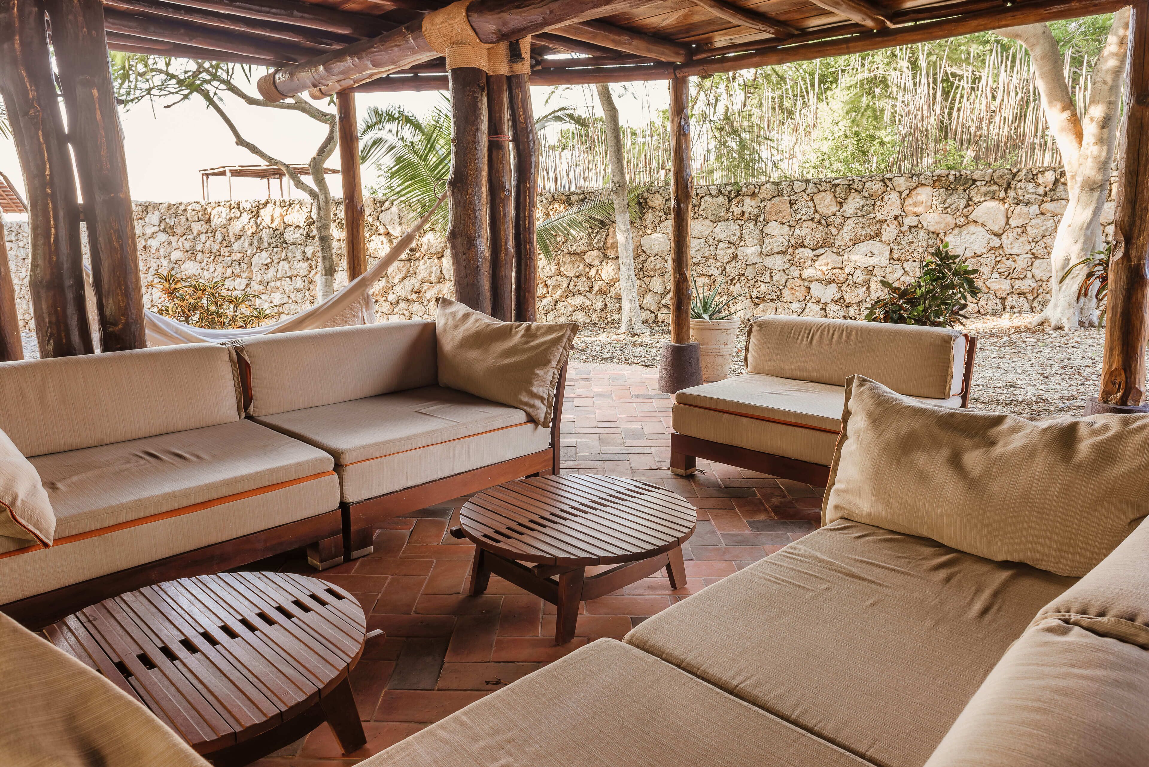A covered outdoor seating area with a stone wall and plants in the background.