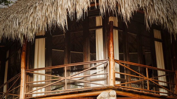A wooden building with a thatched roof, a balcony, and a hammock. - Castillete Hotel & Beach Club (Cartagena)