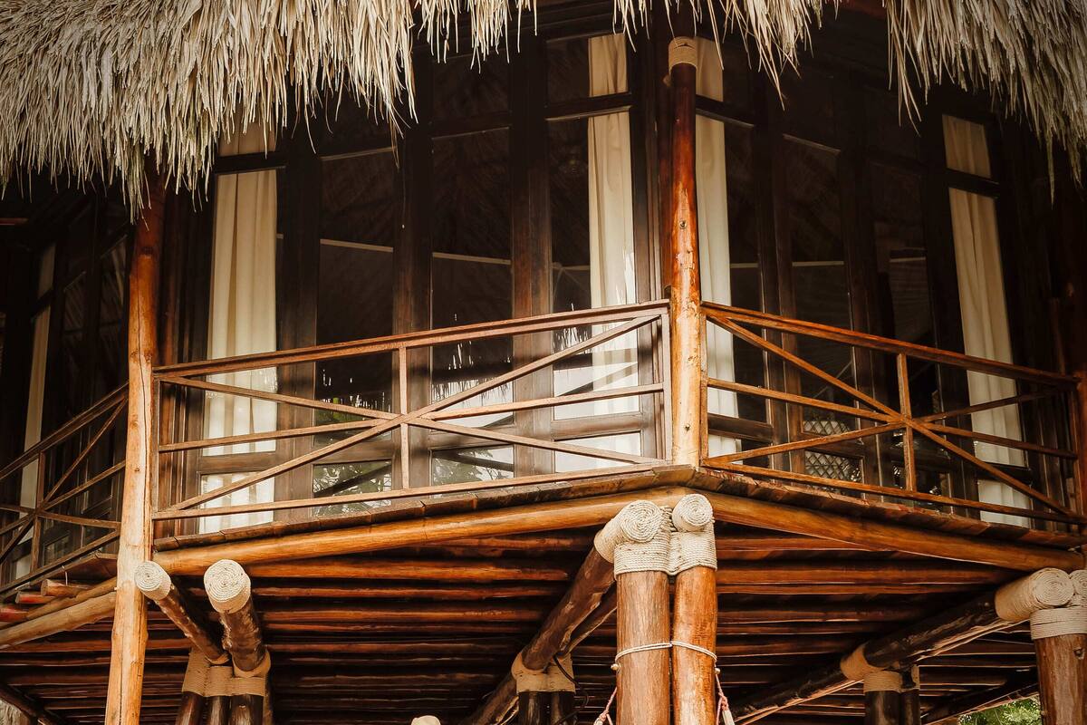 A wooden building with a thatched roof, a balcony, and a hammock.