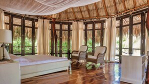A spacious room with a large bed, two wicker chairs, a small white cabinet, and a thatched roof. - Castillete Hotel & Beach Club (Cartagena)