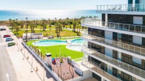 Een modern hotel met een zwembad, uitzicht op de oceaan en een parkeerplaats met auto's.