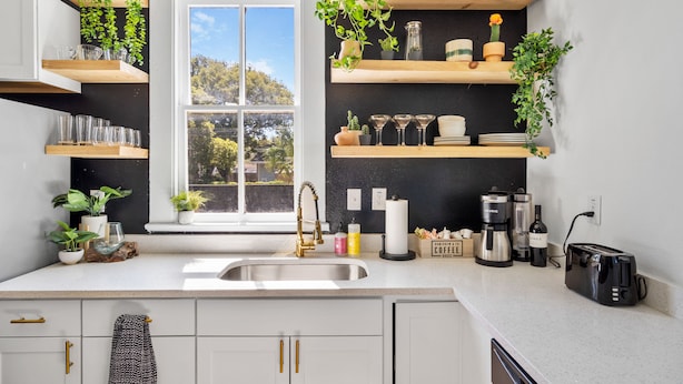 A modern kitchen with white cabinets, wooden shelves, and various kitchen appliances.