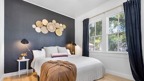 A bedroom with a bed, bedside lamps, a wall art piece, a window with curtains, and a patterned rug.