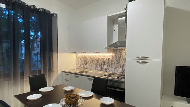 A modern kitchen with white cabinets, a marble backsplash, and a dining table set with white plates and a basket of fruit.