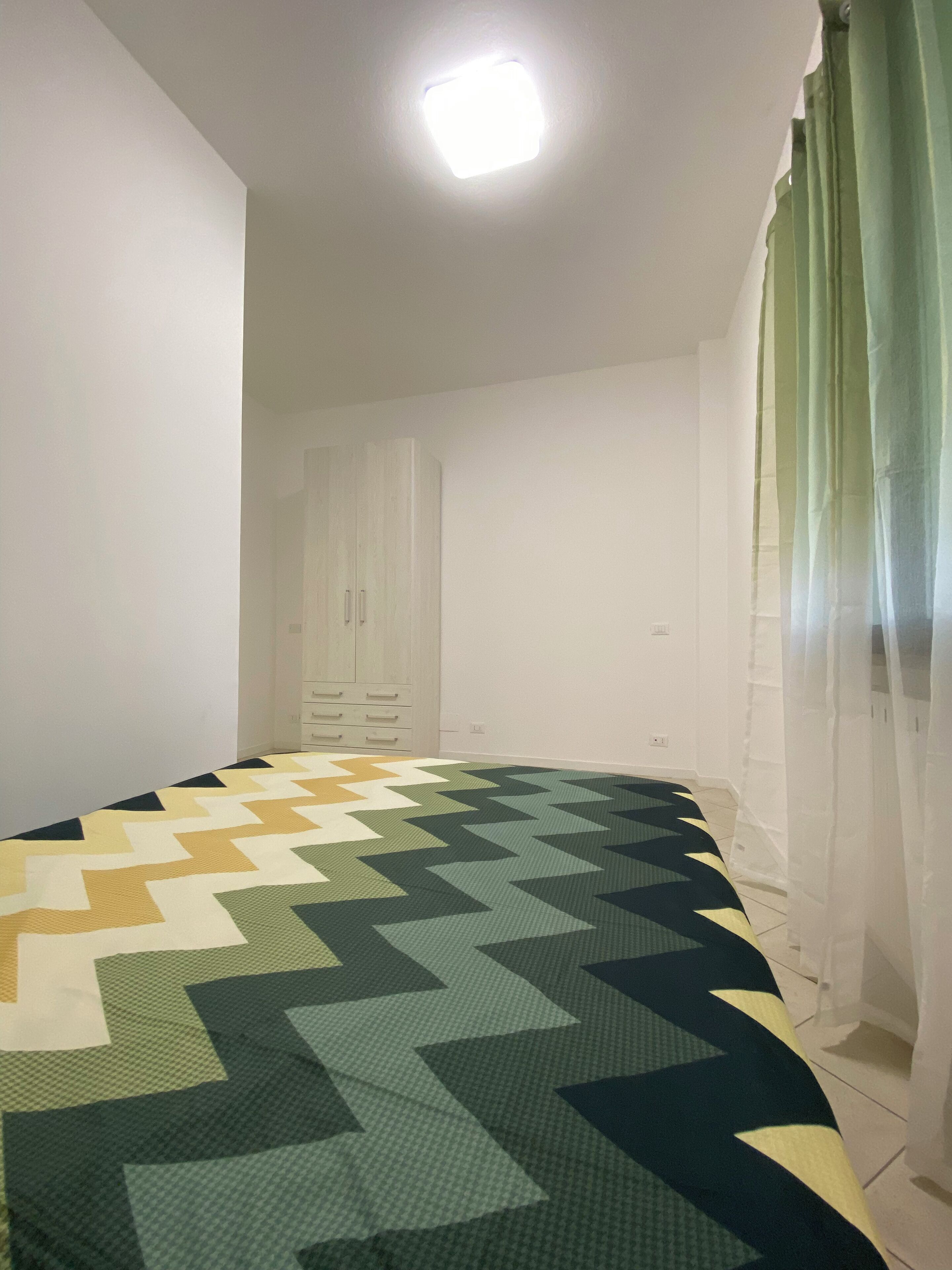 A bedroom with a bed, a wardrobe, and a window with curtains.