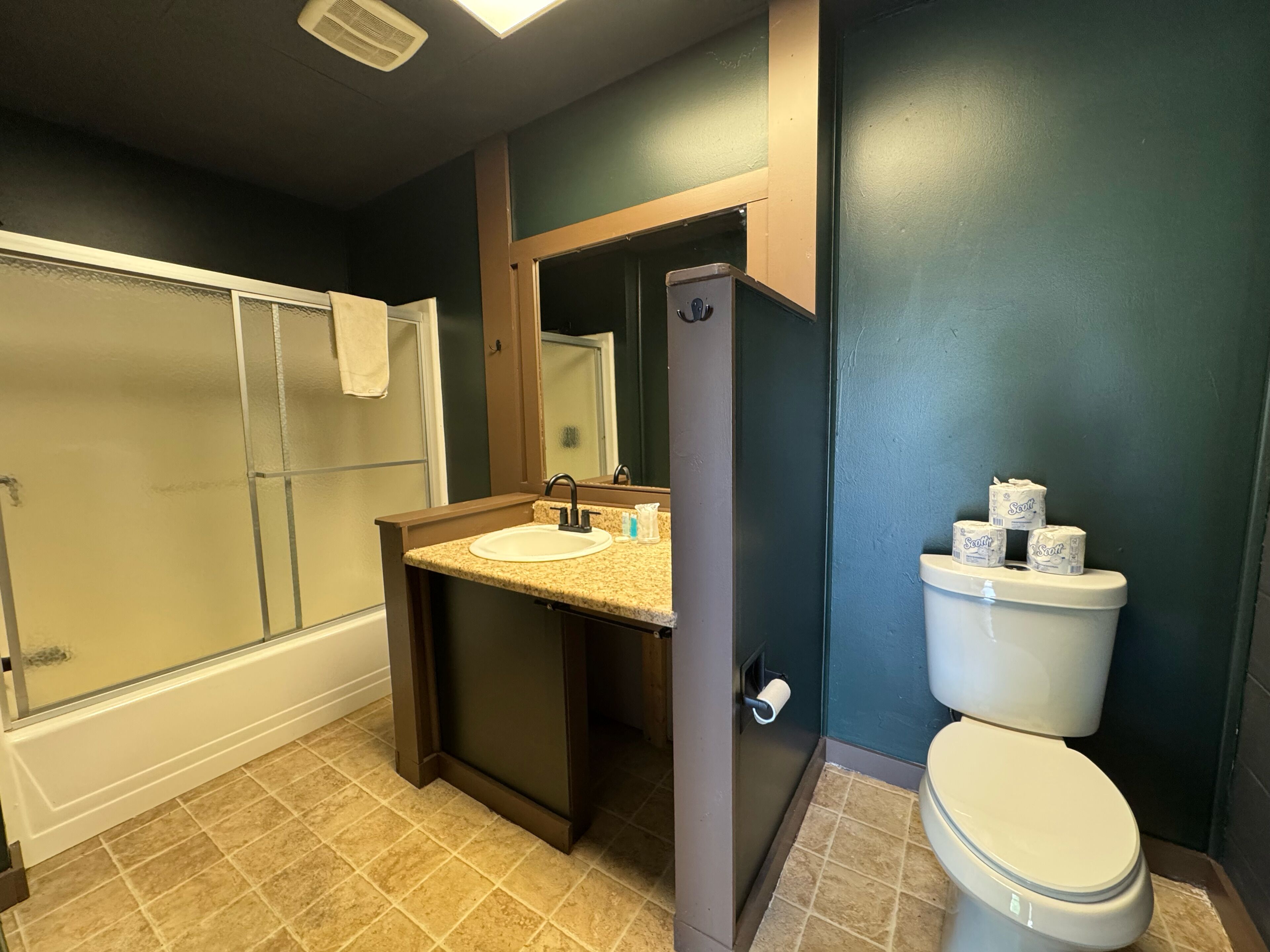 A bathroom with a shower, sink, toilet, and a mirror.