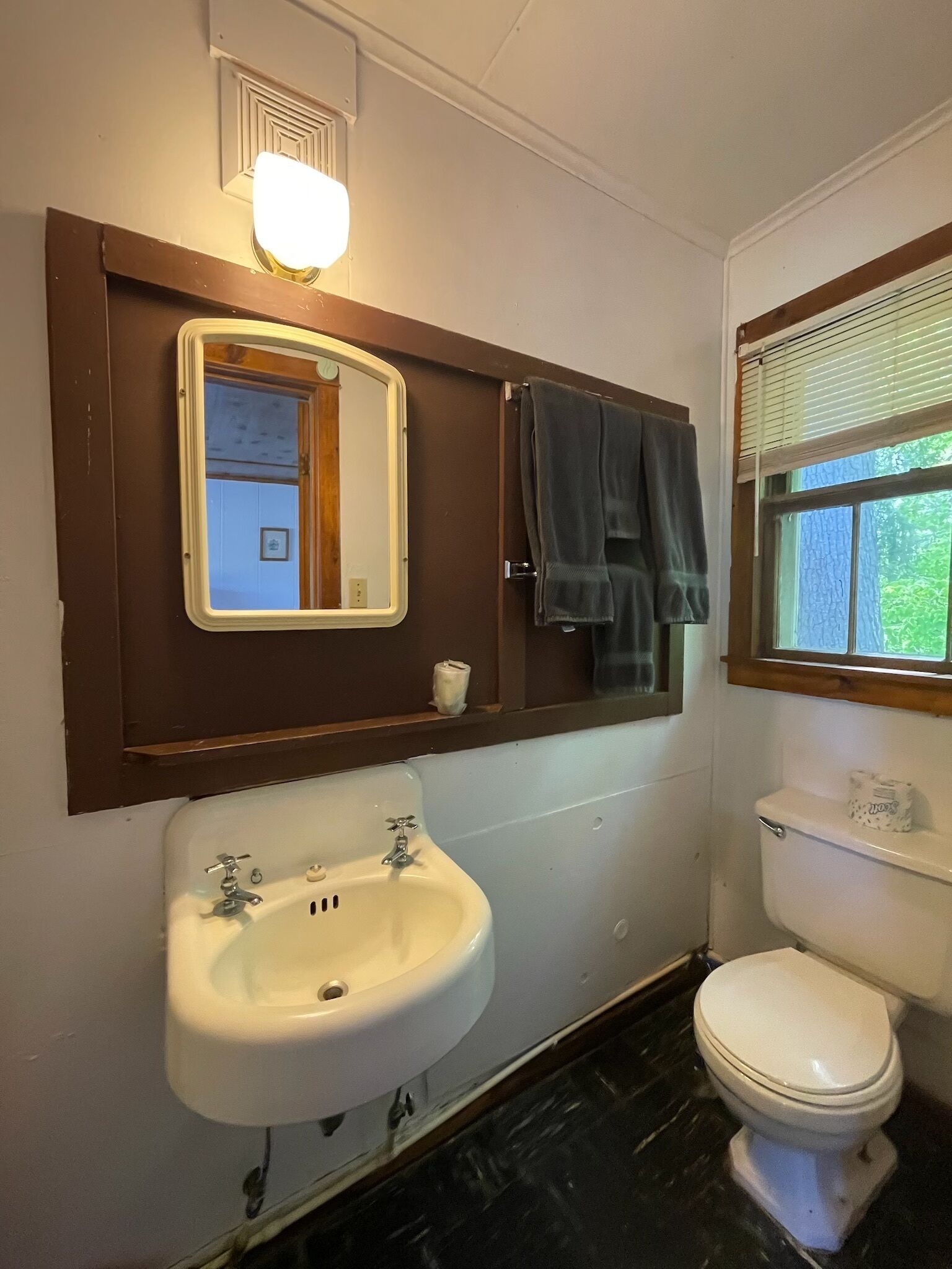A bathroom with a white sink, a mirror, a toilet, and a window with blinds.