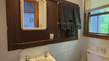 A bathroom with a white sink, a mirror, a toilet, and a window with blinds.