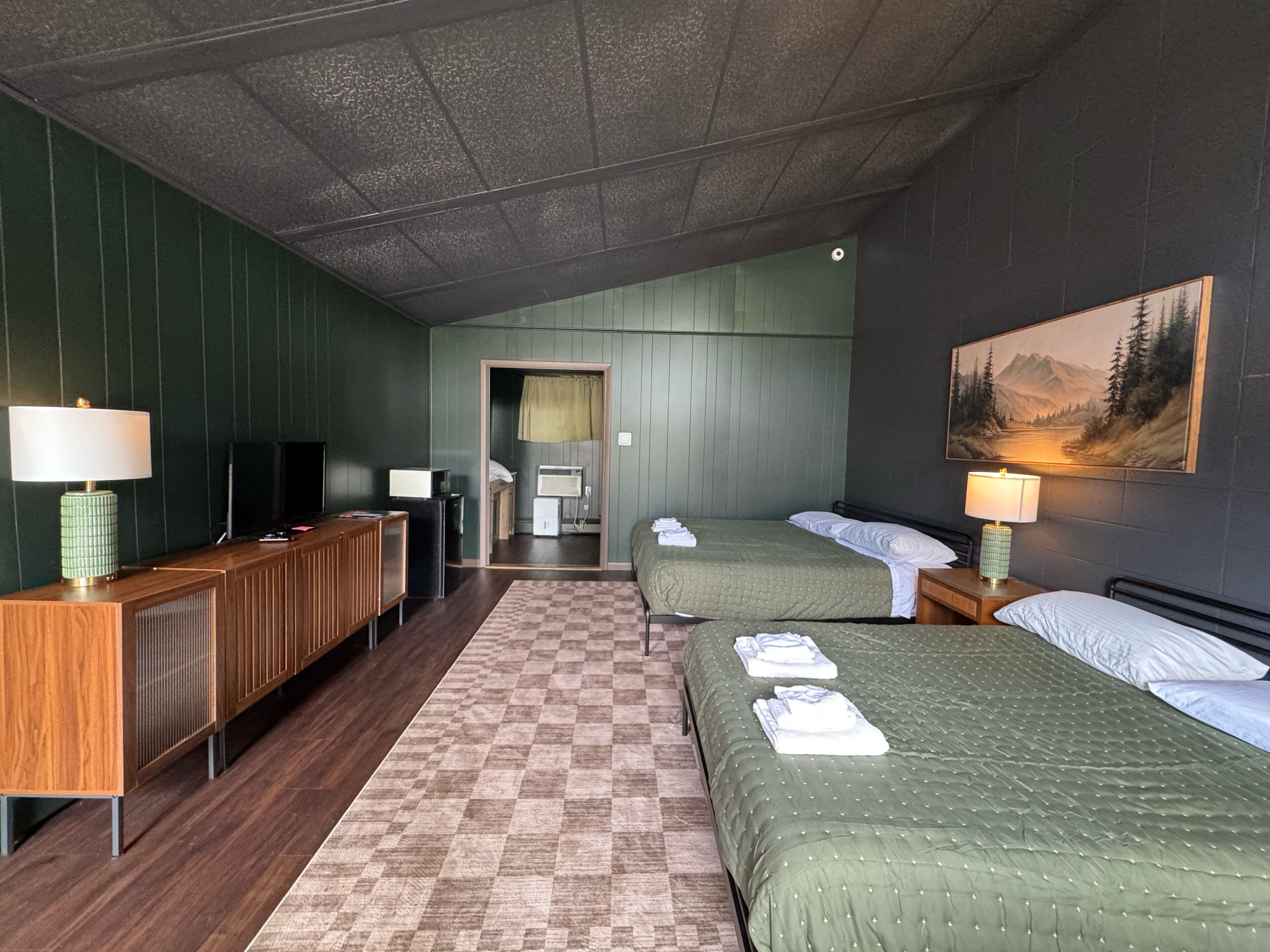 A hotel room with two beds, a desk with a lamp, a television, and a painting on the wall.