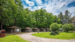 A campground with several wooden cabins, picnic tables, and a playground area surrounded by dense trees.