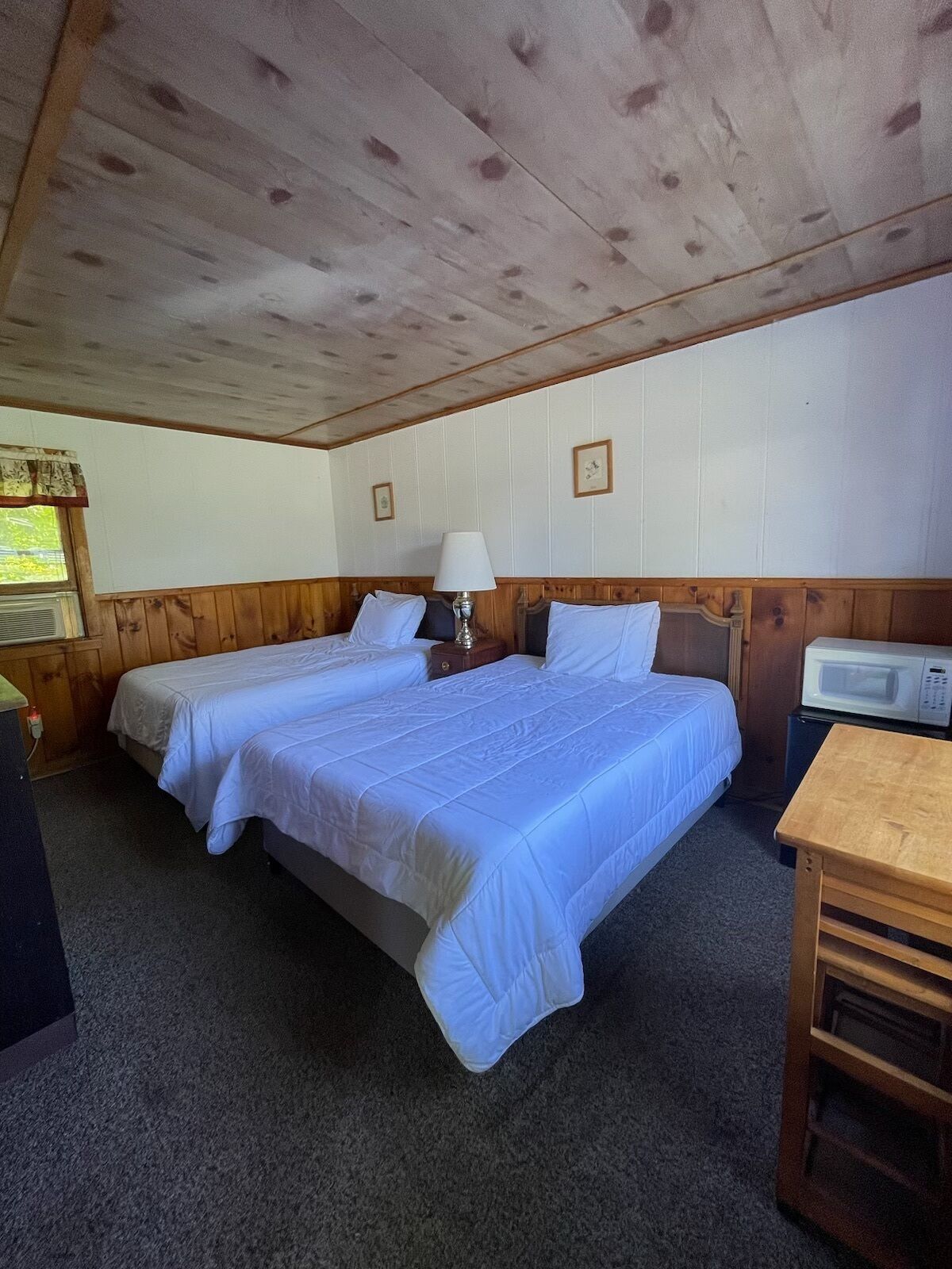 A room with two beds, a table, a lamp, and a microwave.