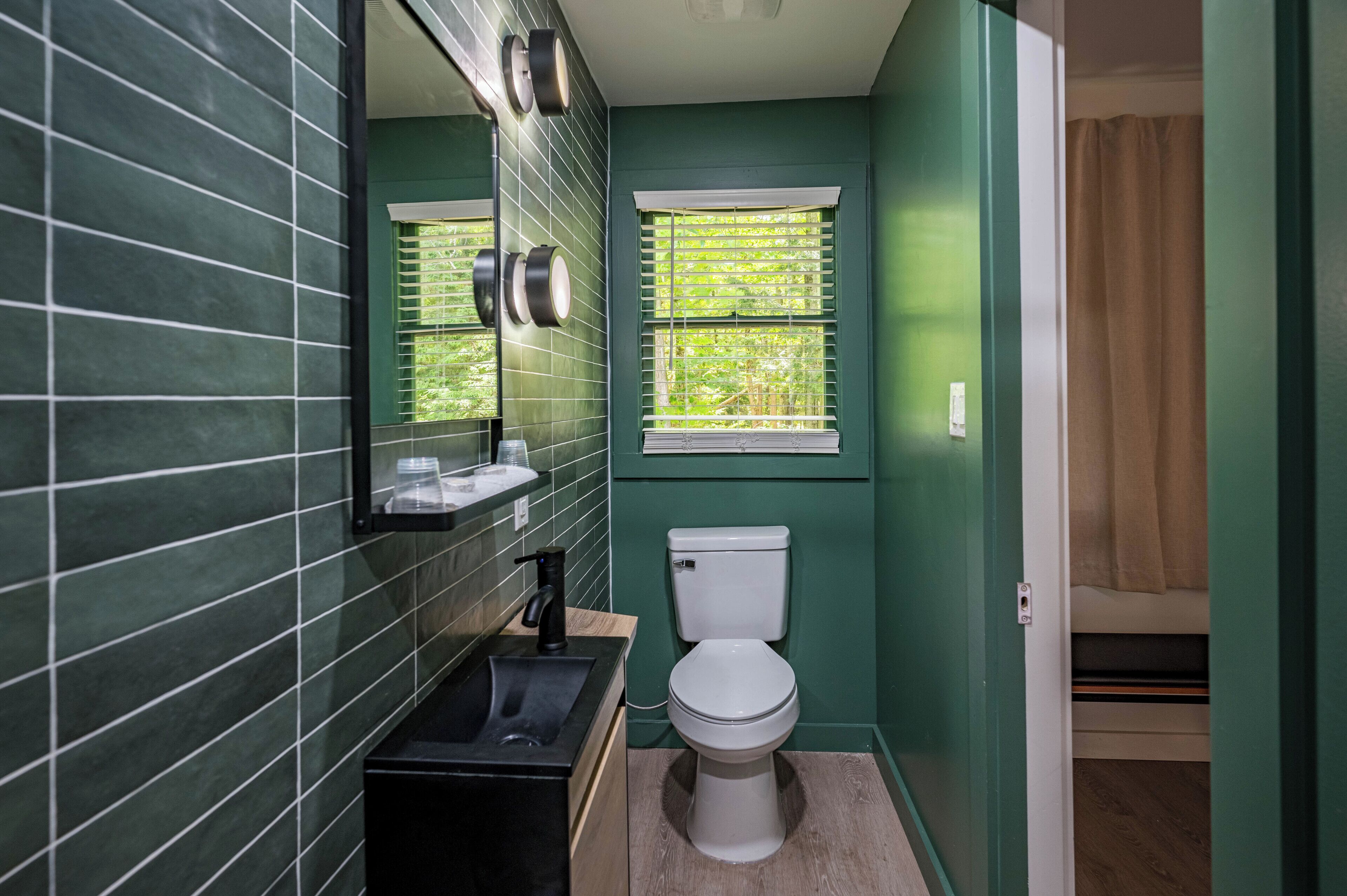 Un baño con inodoro blanco, lavamanos negro y una ventana con persianas.