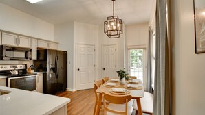 A modern kitchen with white cabinets, stainless steel appliances, and a dining area with wooden chairs and a table set for four. - Shelby Farms Greenline Access: Modern Cordova Home (Cordova)