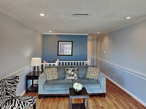 A living room with a blue sofa, a zebra-patterned chair, a small table with a vase, and a picture on the wall. - Bluefish 16 House by Distinctive Beach Rentals (St. Augustine)