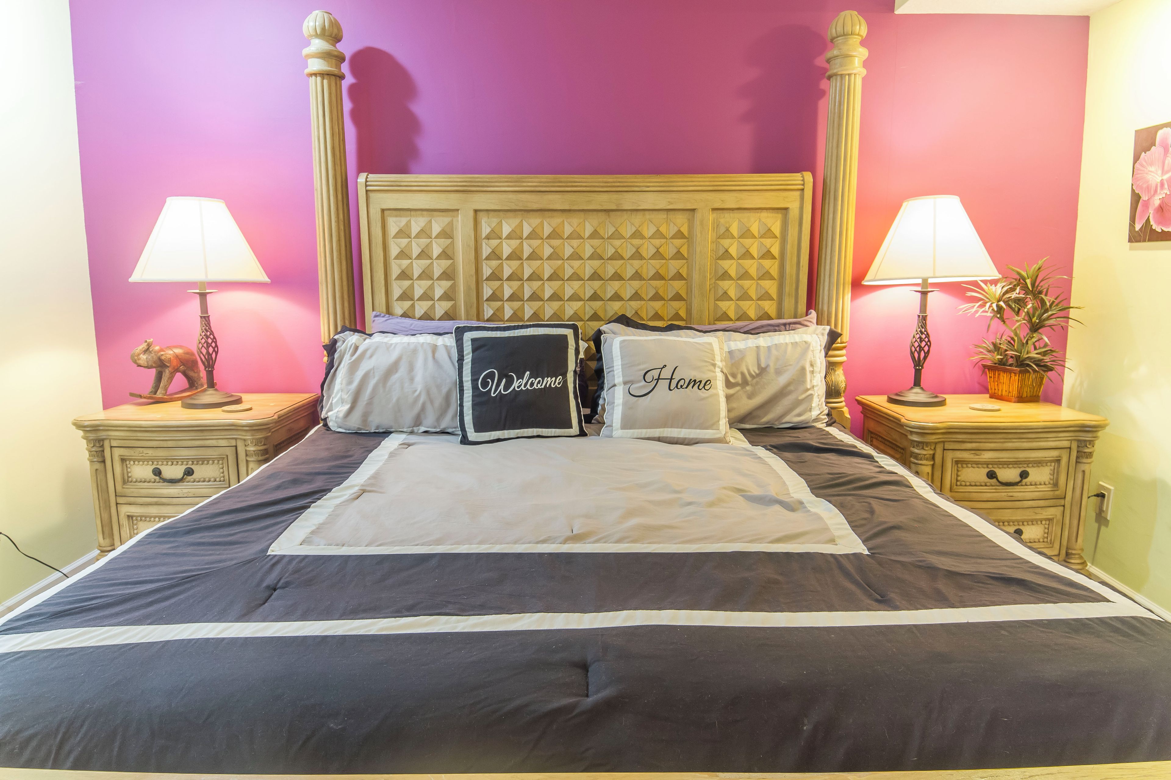A bed with a headboard, two bedside tables, and lamps. There are pillows with "Welcome" and "Home" text.