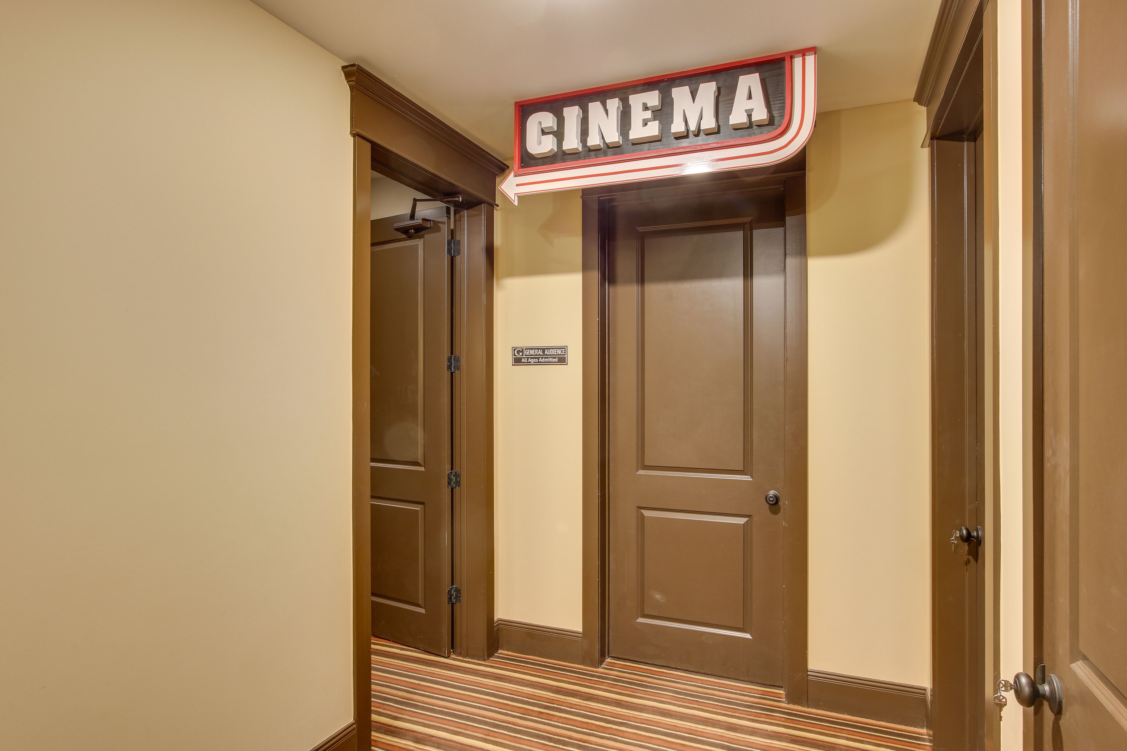 A cinema sign above a set of brown doors with a striped carpet leading to them.