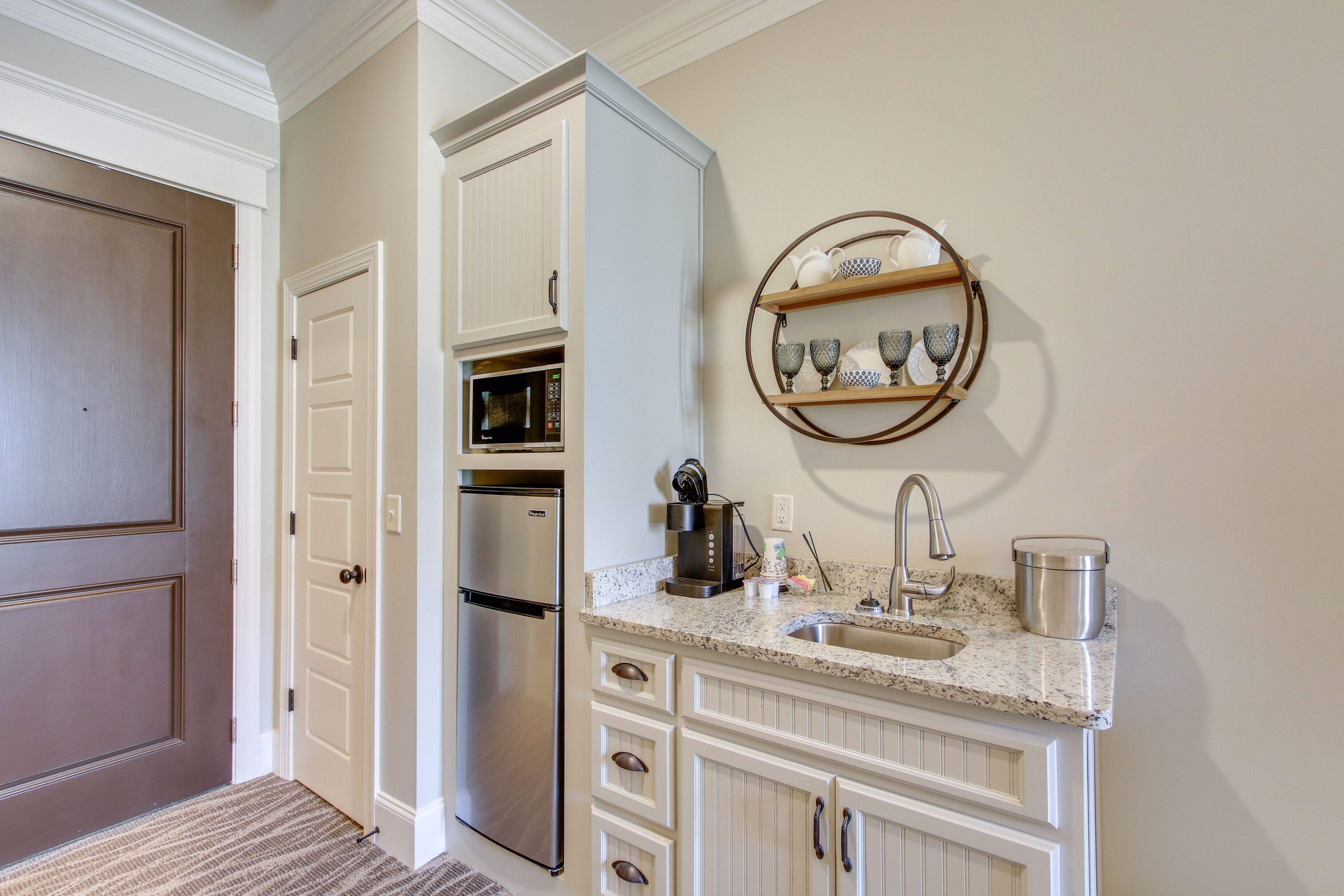 Una cocina con muebles blancos, un refrigerador de acero inoxidable, un microondas, una cafetera y un lavabo con un recipiente de acero inoxidable.