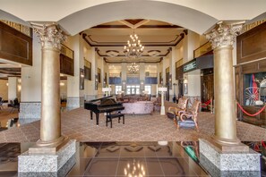 Un'imponente hall con un pianoforte a coda, colonne decorate, un lampadario e un'ampia zona salotto.