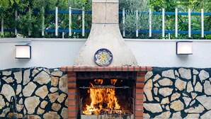 Una xemeneia de maó a l'exterior, amb una paret de pedra i una tanca blava al fons.