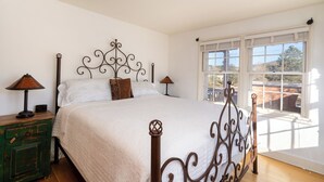 A bedroom with a bed, two bedside tables, a window with a view, and a decorative metal headboard.