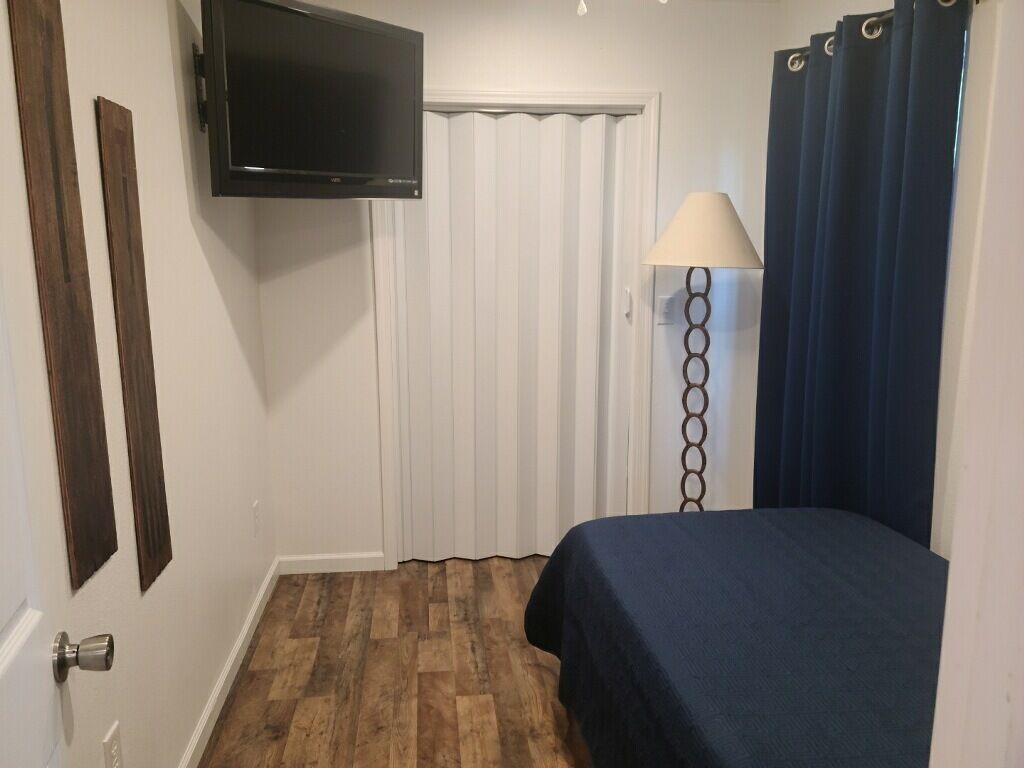 A room with a bed, a television mounted on the wall, a lamp, and a door with curtains.