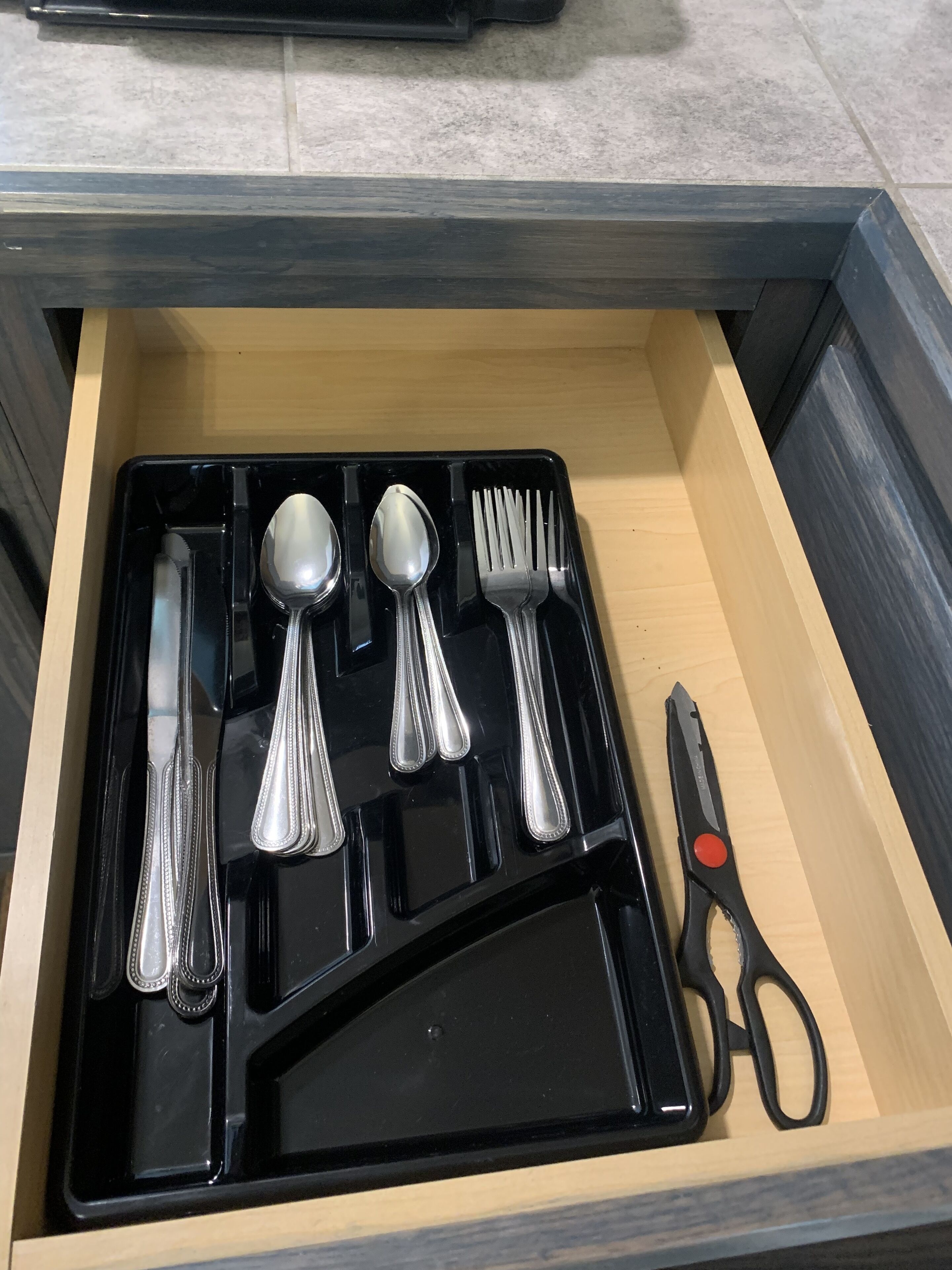 Un cajón con una bandeja negra que contiene un cuchillo, una cuchara, un tenedor y unas tijeras.