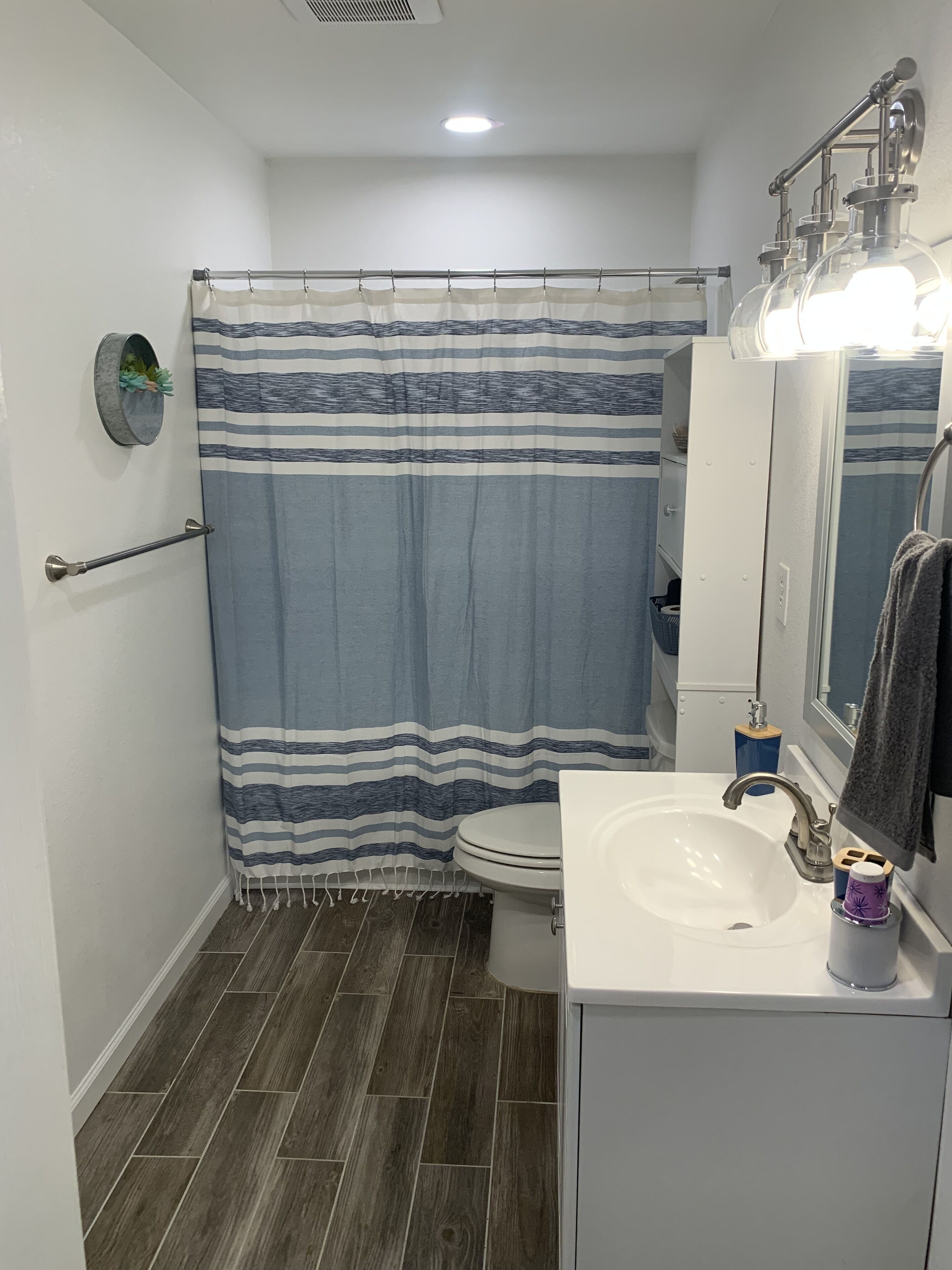 Ein Badezimmer mit gestreifter Duschvorhang, einem weißen Waschbecken mit Spiegel und einem Handtuch an der Wand.