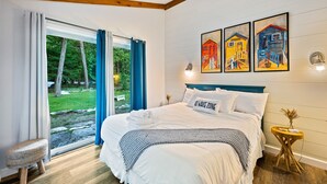 A bedroom with a bed, a bedside table with a lamp, and a window with curtains. - Relax on the Bay — Kayaks, Hot Tub & Firepit Nights (Ellison Bay)