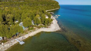 An aerial view of a coastal area with a clear shoreline, a dock, and a forested hill. - Relax on the Bay — Kayaks, Hot Tub & Firepit Nights (Ellison Bay)