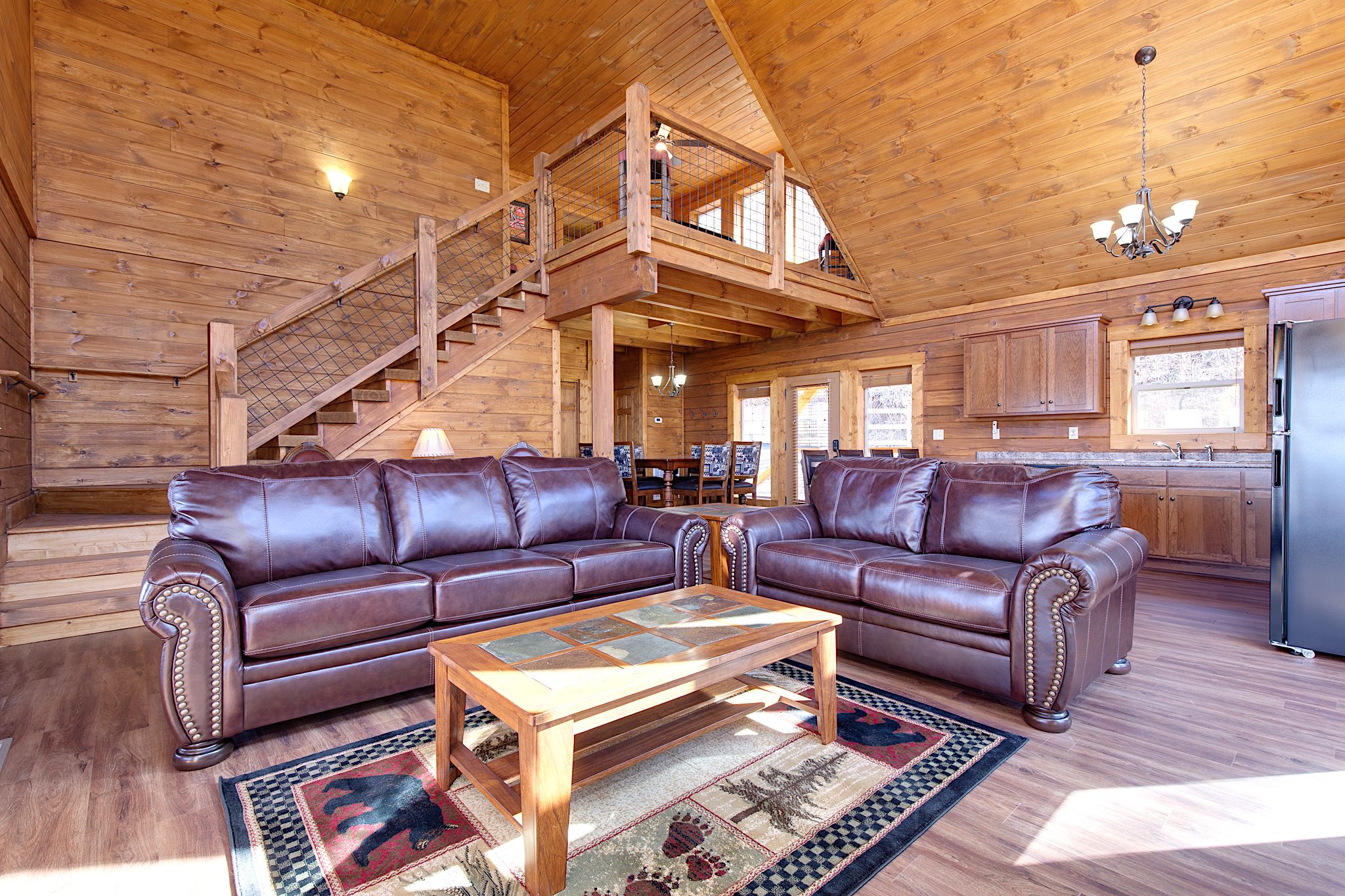 A spacious living room with a large brown leather sectional sofa, a wooden coffee table, and a staircase leading to an upper level.