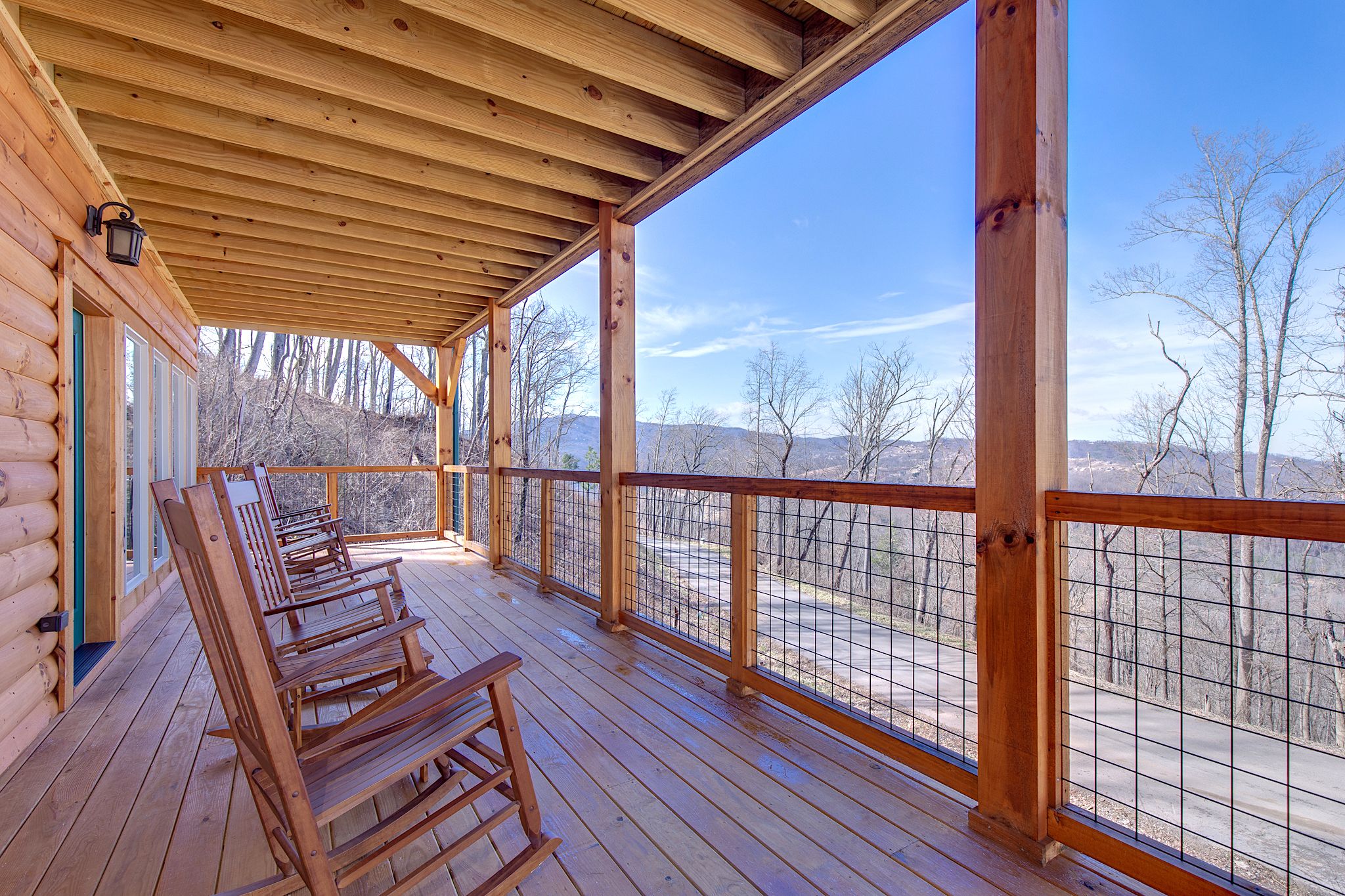 A wooden deck with a railing, wooden chairs, and a view of a mountainous landscape.