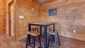 Een houten interieur met een houten tafel en krukken, een bord aan de muur en een deur.