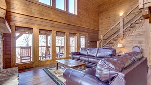 A spacious living room with a large wooden ceiling, a stone fireplace, and a staircase. - Lasting Impressions by Jackson Mountain Rentals (Gatlinburg)