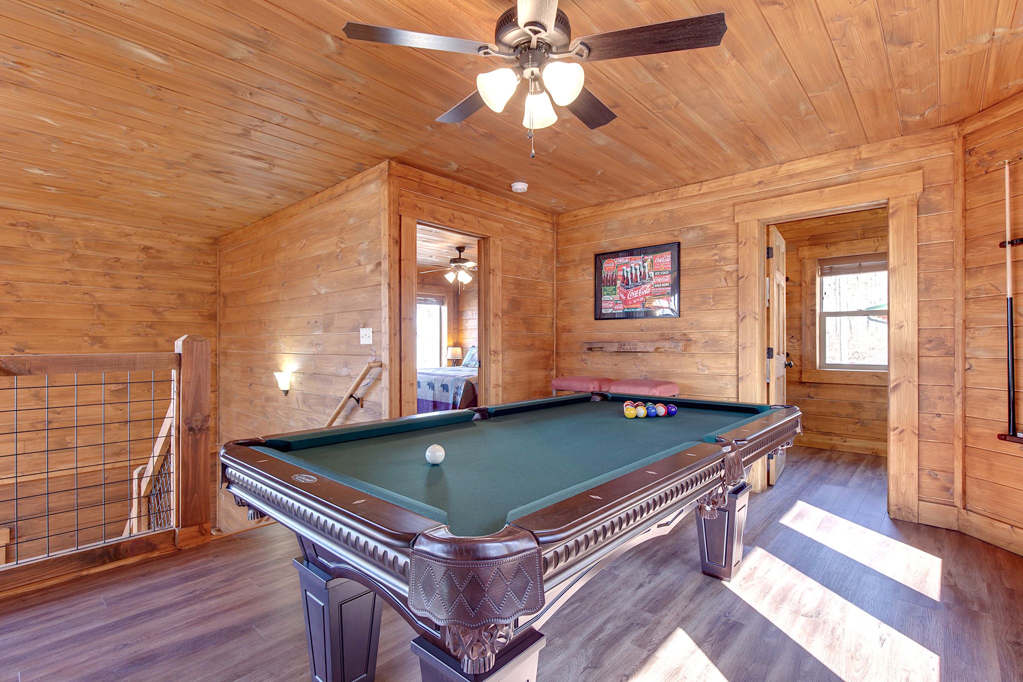 A pool table in a wooden room with a ceiling fan, a framed picture on the wall, and a window.