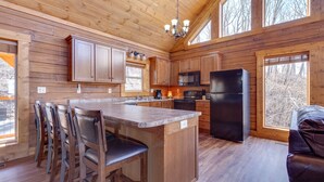 A wooden cabin kitchen with a central island, bar stools, and a refrigerator. - Lasting Impressions by Jackson Mountain Rentals (Gatlinburg)