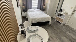 Habitación de hotel pequeña con cama, mesitas de noche, un rincón de descanso con una mesa para dos personas y un armario.