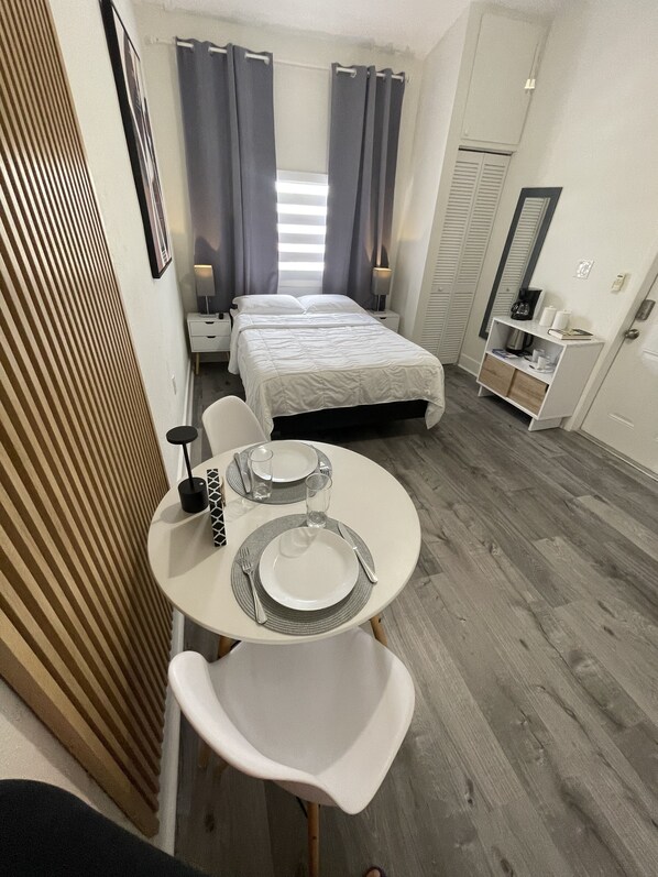 Une chambre d’hôtel compacte comprenant un lit, des tables de chevet, un petit coin salon avec une table préparée pour deux personnes et une armoire.